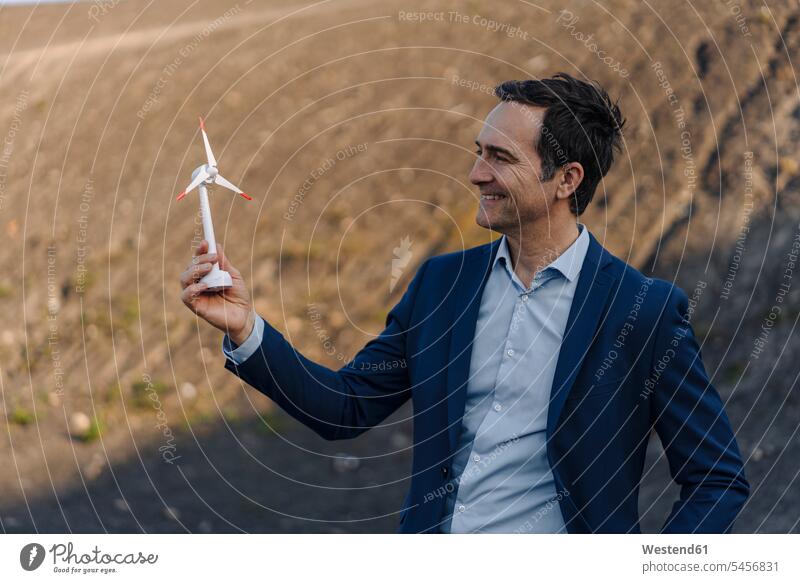 Happy mature businessman on a disused mine tip holding wind turbine model human human being human beings humans person persons caucasian appearance