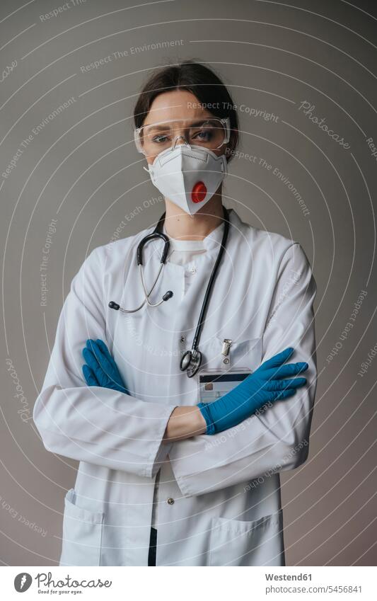 Female doctor wearing mask and protective eyewear with arms crossed standing against wall in hospital color image colour image indoors indoor shot indoor shots
