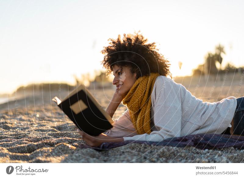 Woman lying in the sand, relaxing on the beach, reading a book relaxation relaxed mid adult women mid adult woman mid-adult women mid-adult woman beaches sandy