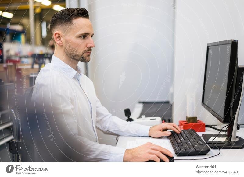 Businessman using computer at desk in a factory computers Business man Businessmen Business men factories business people businesspeople business world