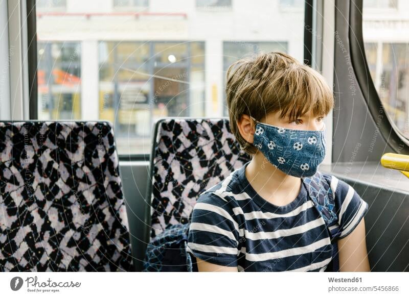 Boy wearing protective mask in tram balls football footballs soccer balls railroad railroads Railways streetcar streetcars trams tramways Seated sit hygienic