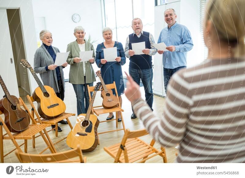 Seniors in retirement home making music singing in choir choirs chorus Instrument Instruments musical instruments guitars chairs learn smile exercise exercising