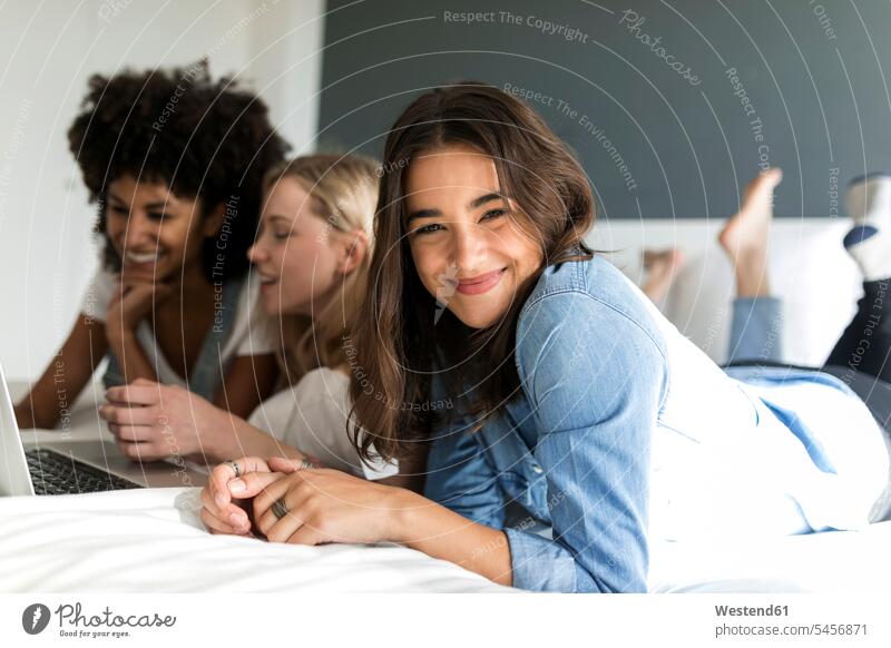 Portrait of smiling young woman lying with girlfriends on bed using laptop females women Laptop Computers laptops notebook laying down lie lying down