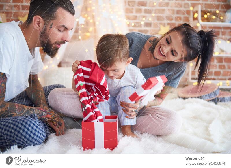 Boy opening Christmas present with his parents in bed Christmas presents family families christmas time yule-tide yuletide X-Mas Xmas X mas beds gift gifts