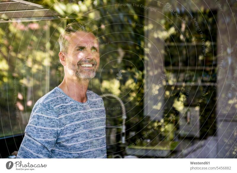 Portrait of smiling mature man behind windowpane at home window glass window glasses windowpanes Window Pane portrait portraits men males windows Adults