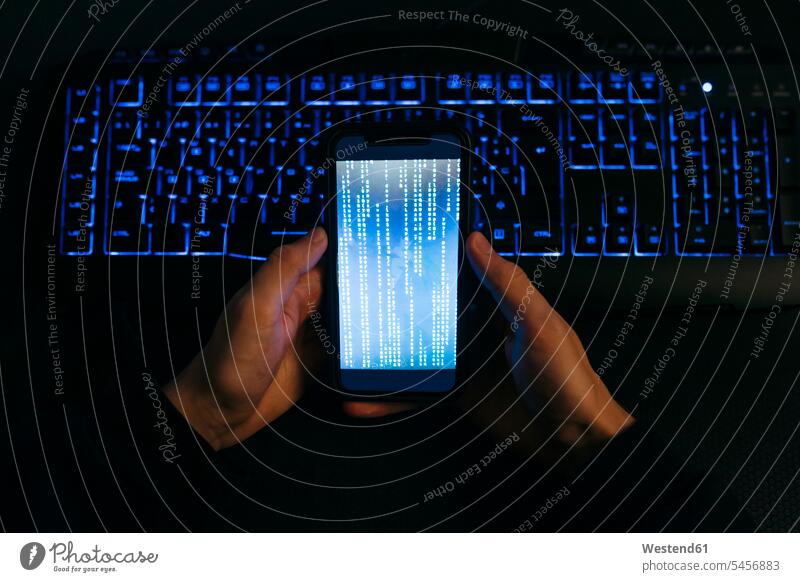 Computer hacker hand holding mobile phone against computer keyboard at office color image colour image indoors indoor shot indoor shots interior interior view