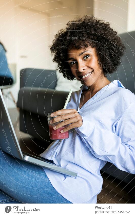 Portrait of smiling woman with soft drink sitting on floor using laptop floors refreshing drink soft drinks refreshing drinks happiness happy females women