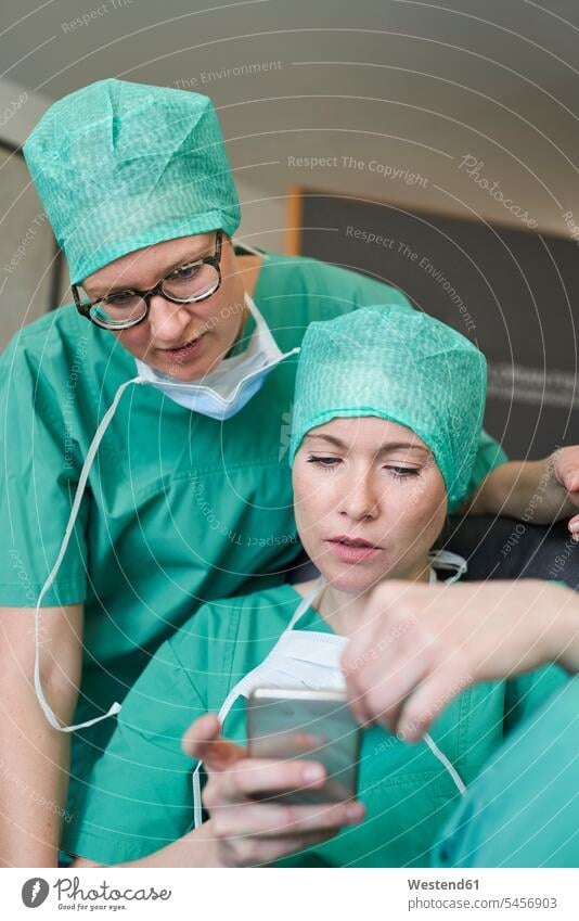 Two women in scrubs looking at cell phone health Germany using use occupation profession professional occupation jobs Protection protecting together hospital