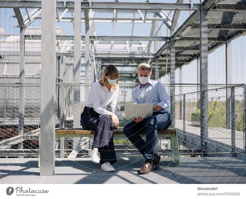 Colleagues wearing masks discussing over laptop while sitting on seat in greenhouse color image colour image Germany business people businesspeople