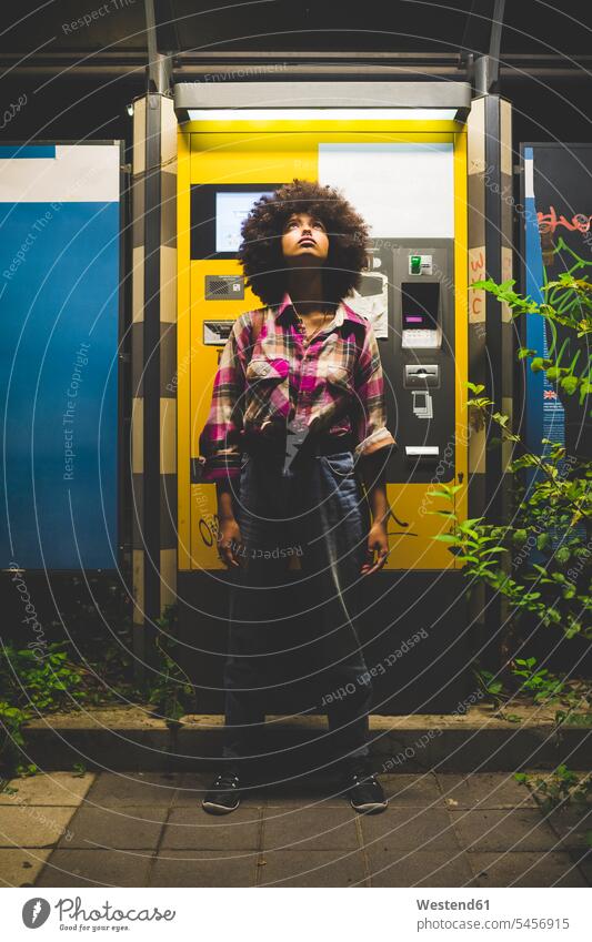Young woman with afro hairdo standing at ticket machine at night looking up human human being human beings humans person persons curl curled curls curly hair