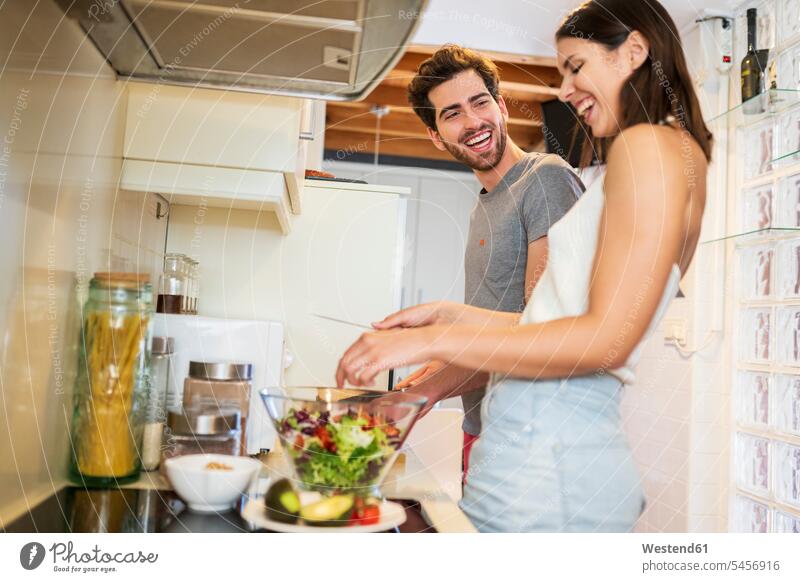 Cheerful young couple preparing meal together in kitchen at home color image colour image Spain friendship bonding community leisure activity leisure activities