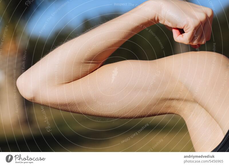 Cropped photo of young woman's arm with muscles, biceps on nature background. Girl close up of demonstrates strong hand after workout, fitness, sport activities outdoors. World heath day