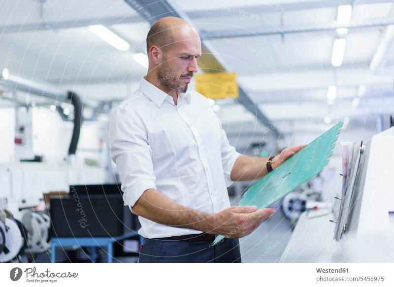 Confident mature male engineer analyzing large circuit board at illuminated factory color image colour image indoors indoor shot indoor shots interior