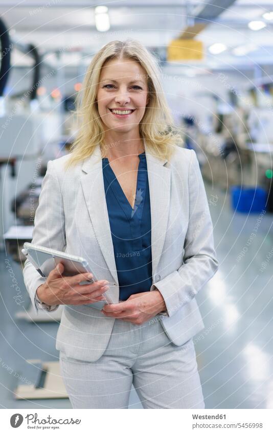 Smiling mature blond businesswoman holding digital tablet while standing at illuminated industry color image colour image indoors indoor shot indoor shots