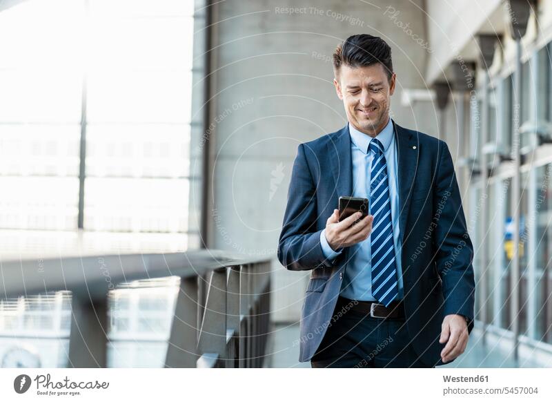 Smiling businessman with cell phone on the move walking going Businessman Business man Businessmen Business men on the way on the go on the road mobile phone