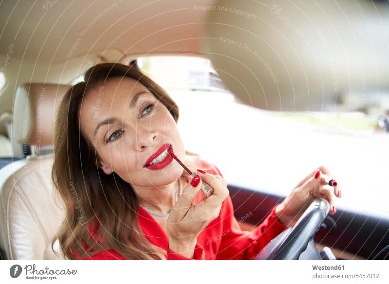 Portrait of mature woman applying lipp gloss in car dresses driving mirror Rear Mirror rear view mirror rearview mirror motor vehicles road vehicle