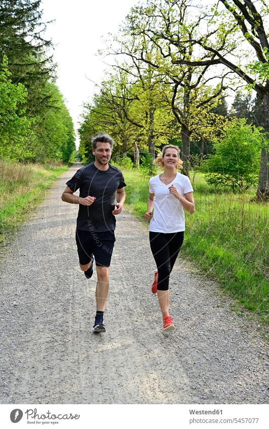 Happy couple jogging on dirt road against trees and plants in forest color image colour image Germany wood woods forests nature natural world the natural world