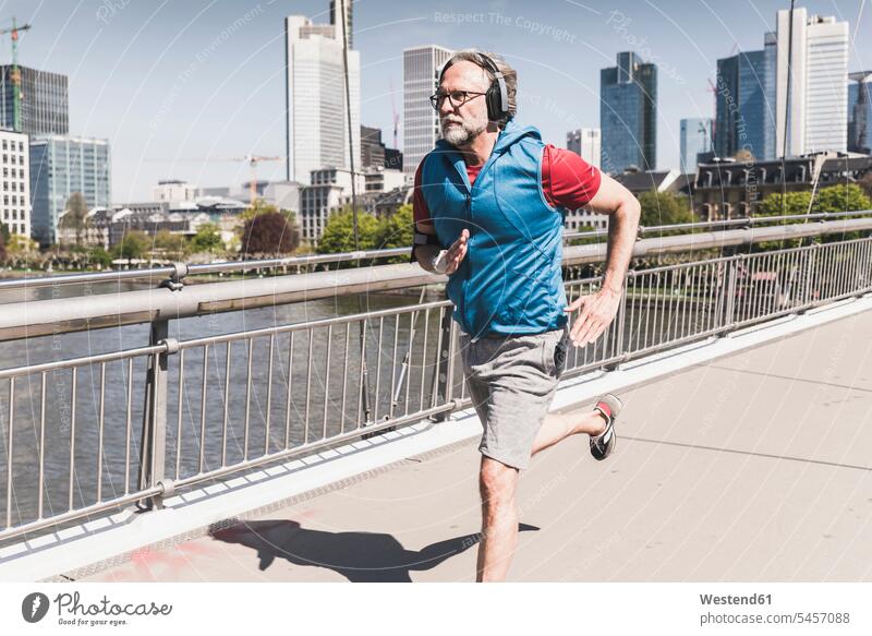 Mature man with headphones running on bridge in the city men males bridges town cities towns headset Adults grown-ups grownups adult people persons human being