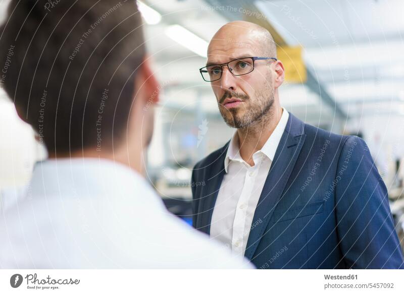 Confident bald businessman looking at young male technician in factory color image colour image indoors indoor shot indoor shots interior interior view