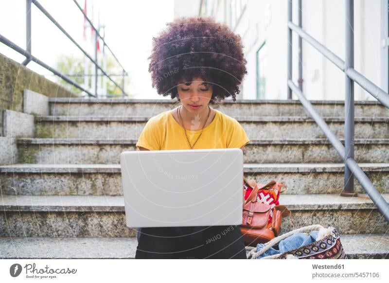 Young woman with afro hairdo using laptop on stairs in the city human human being human beings humans person persons curl curled curls curly hair back-pack
