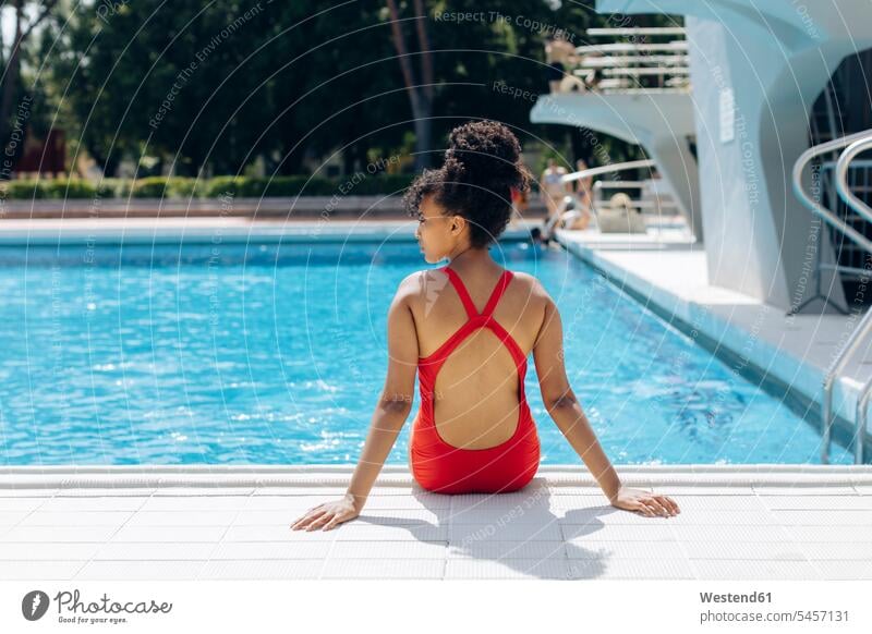Back view of young woman wearing red swimsuit sitting at poolside tiles swim wear bathing costume bathing costumes bathing suit bathing suits Swimming Costume