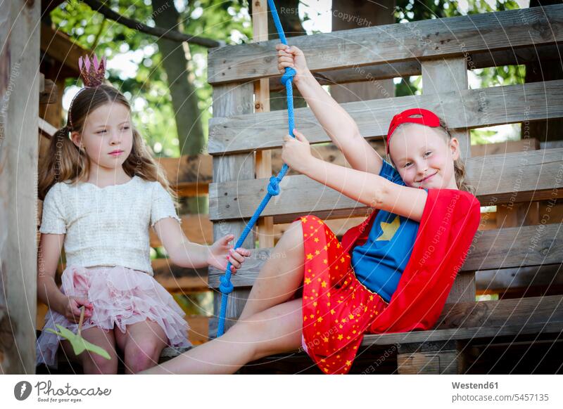 Girls dressed up as princess and superwoman playing in a tree house human human being human beings humans person persons braver bravers hero skirts crowns ropes
