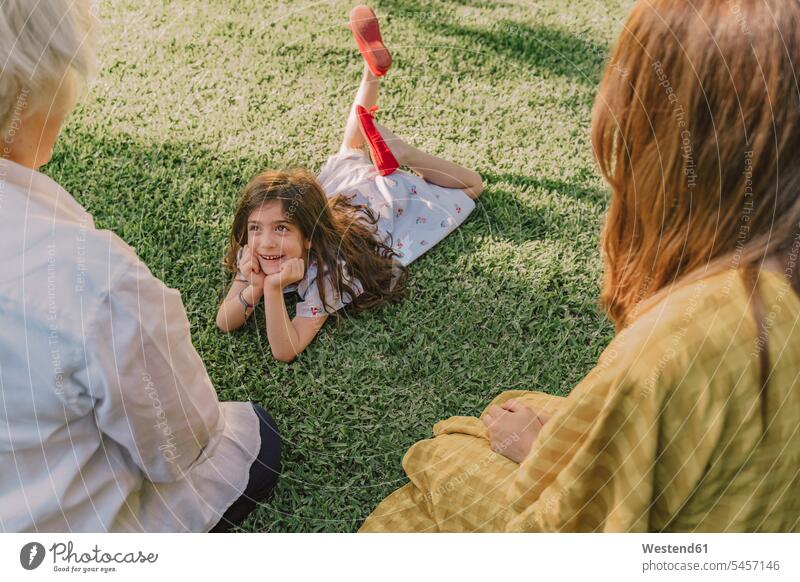 Cute girl with hands on chin talking with family while lying over grassy land in yard color image colour image Spain leisure activity leisure activities