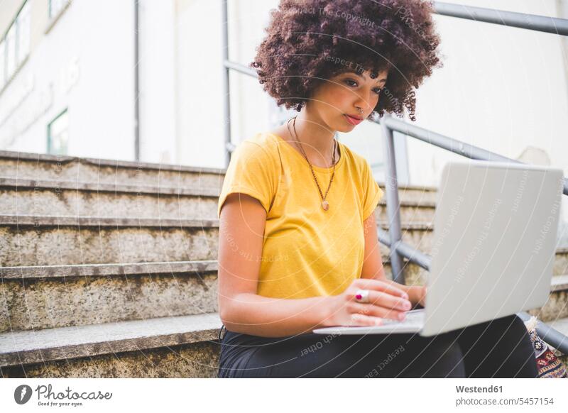 Young woman with afro hairdo using laptop on stairs in the city human human being human beings humans person persons curl curled curls curly hair T- Shirt