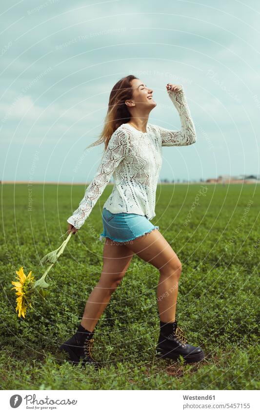 Young woman walking, holding a sunflower in a green field going Freedom Liberty free Harmony Harmonious Sunflower Helianthus annuus Sunflowers happiness happy