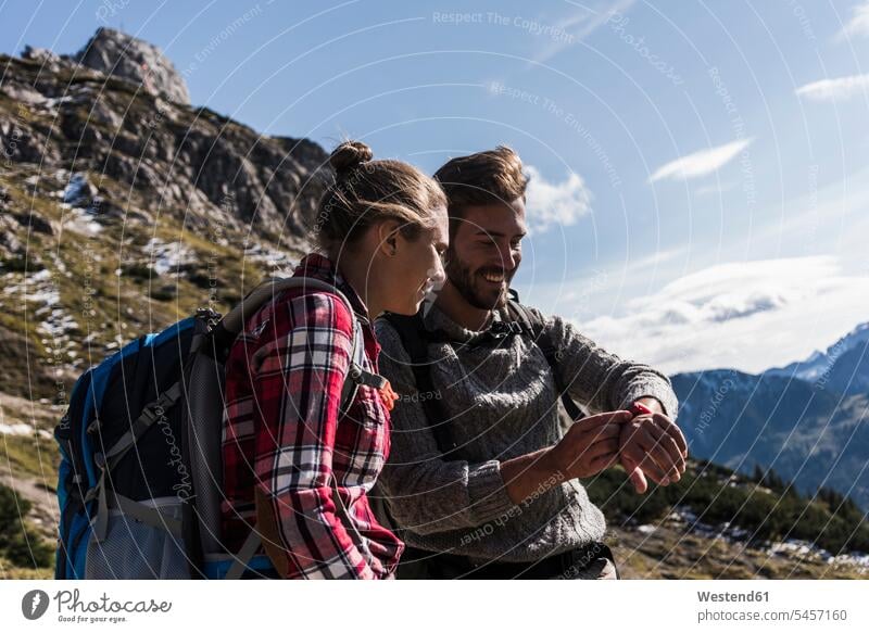 Austria, Tyrol, smiling young couple looking at watch in mountainscape hiking hike twosomes partnership couples smile eyeing wrist watch Wristwatch Wristwatches