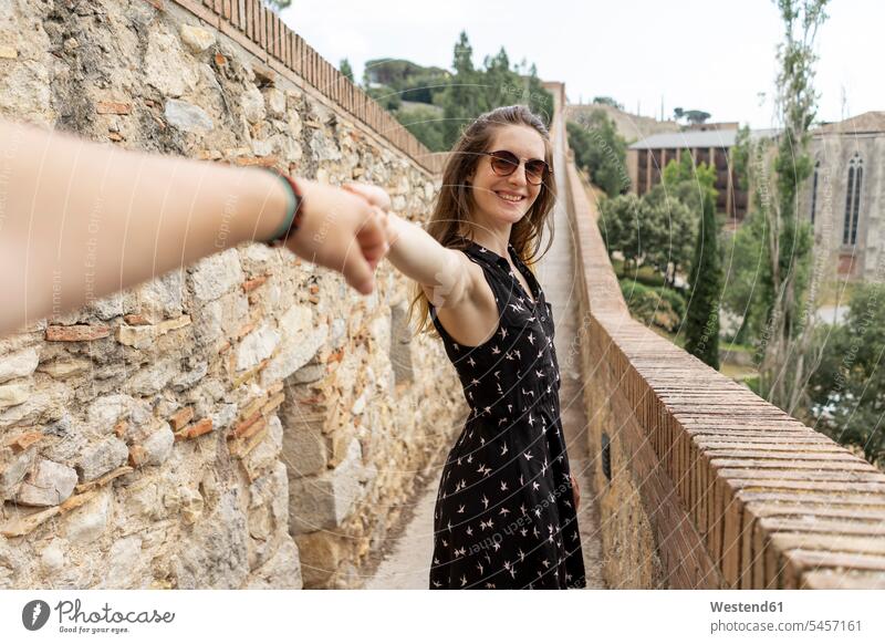 Spain, Girona, smiling woman holding man's hand walking along stone wall stonewalls smile females women Town going human hand hands human hands Adults grown-ups