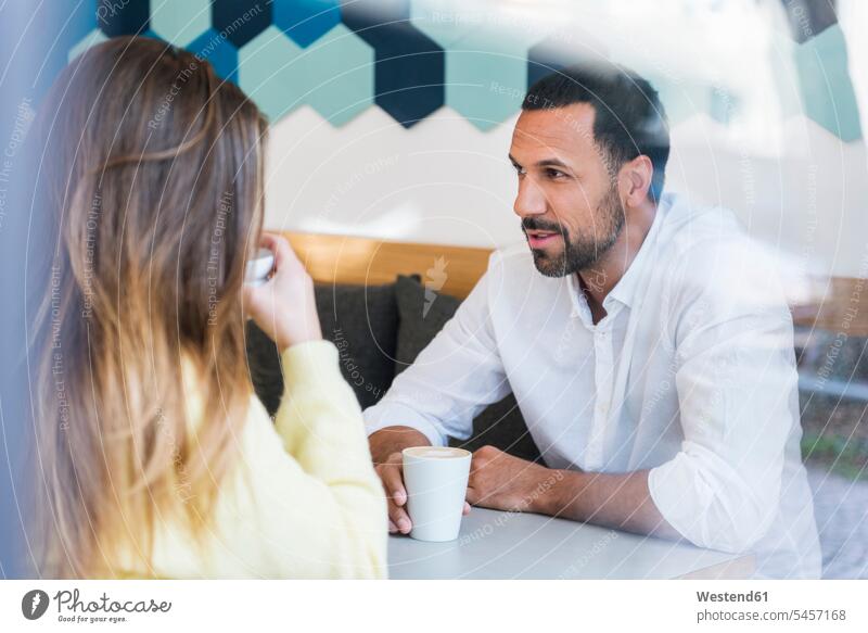 Man and woman sitting in a cafe talking men males speaking Seated couple twosomes partnership couples females women Adults grown-ups grownups adult people
