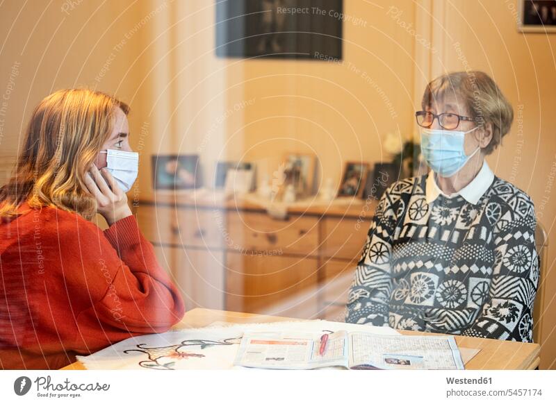 Granddaughter and mother wearing face mask talking while sitting with social distance at home during Covid-19 color image colour image day daylight shot