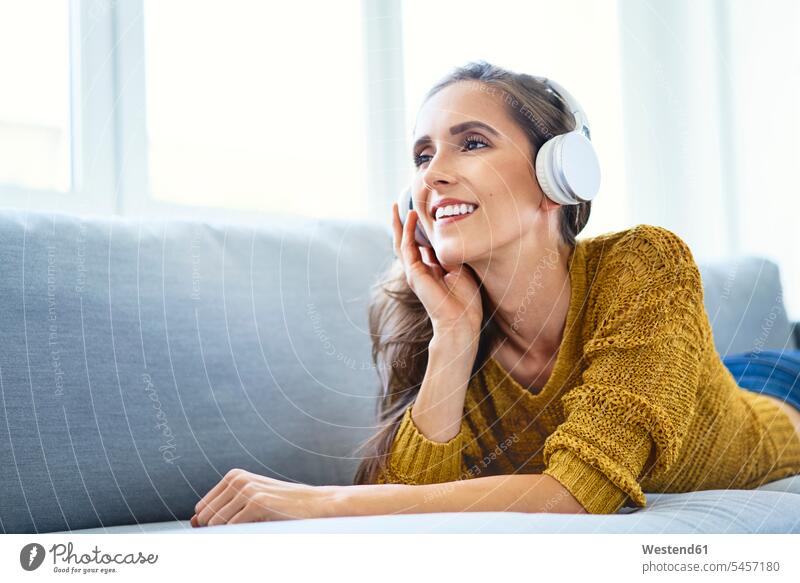 Happy young woman listening to music with headphones while lying on sofa human human being human beings humans person persons celibate celibates singles