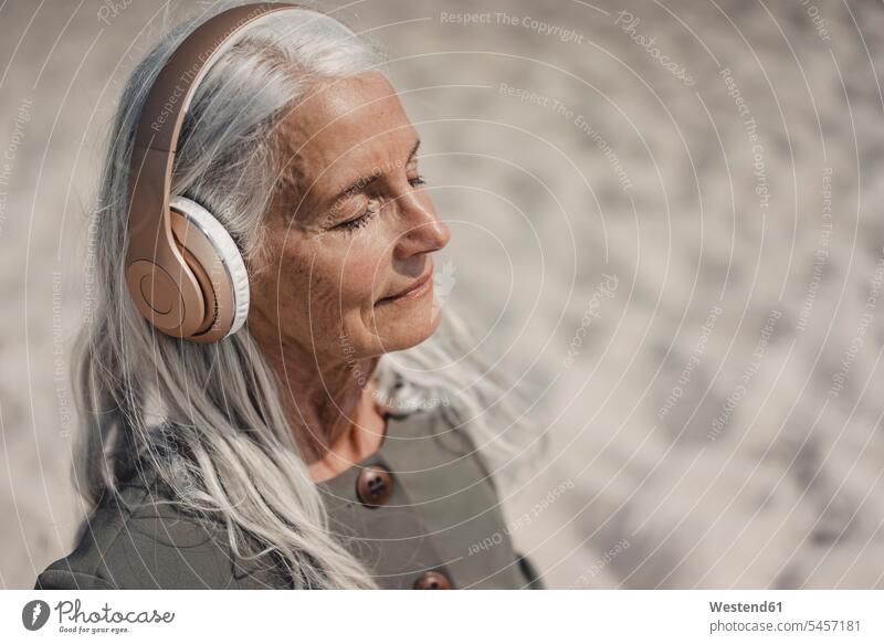 Senior woman listening music with headphones on the beach human human being human beings humans person persons caucasian appearance caucasian ethnicity european
