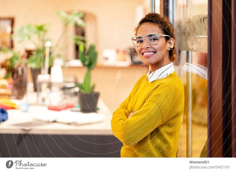 Young woman standing in door of a fashion store, smiling young women young woman fashion shop boutique fashion boutique smile glasses specs Eye Glasses