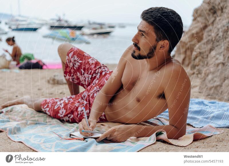 Young man lying on towel at the beach, notebook, thoughtful laying down lie lying down thinking diary diaries beard pensive Reflective contemplative men males