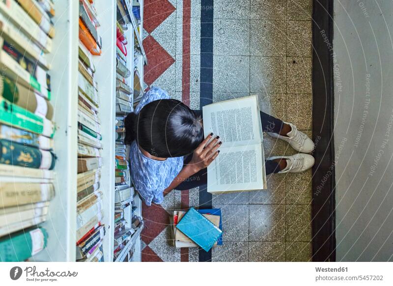 Top view of young woman sitting on the floor reading a book at National library, Maputo, Mocambique books rack racks Shelve shelves book shelf Book Shelves
