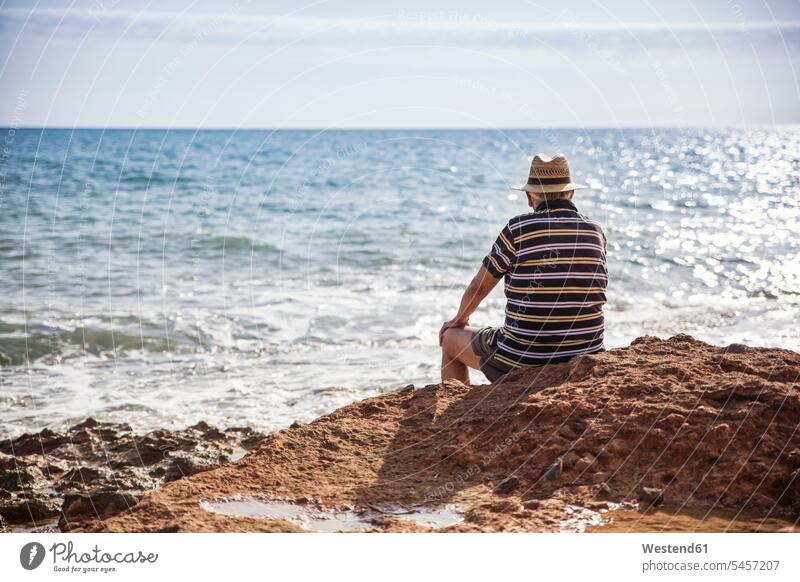 Italy, Sicily, Cava D'aliga, senior man sitting at the coast and looking to the sea ocean view seeing viewing coastline shoreline men males Seated senior men