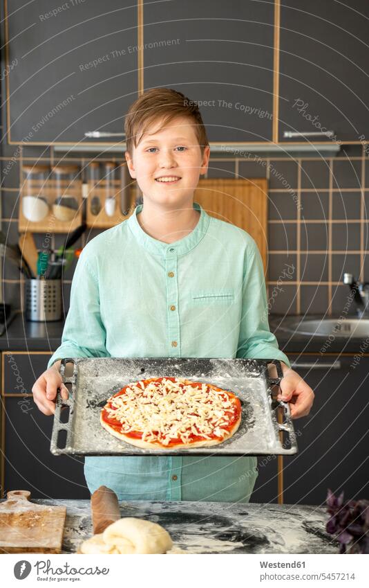 Portrait of smiling boy holding baking tray with raw homemade pizza shirts bake smile delight enjoyment Pleasant pleasure happy stand at home free time