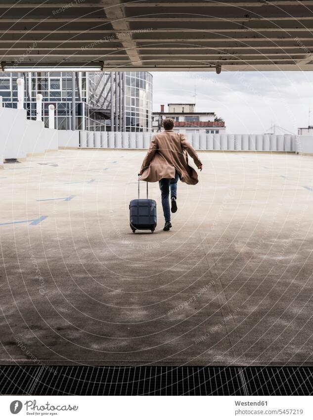 Businessman with rolling suitcase in a hurry at parking garage rolling suitcases parking garages parking deck Hurry rushing Urgency urgent hurrying In A Hurry