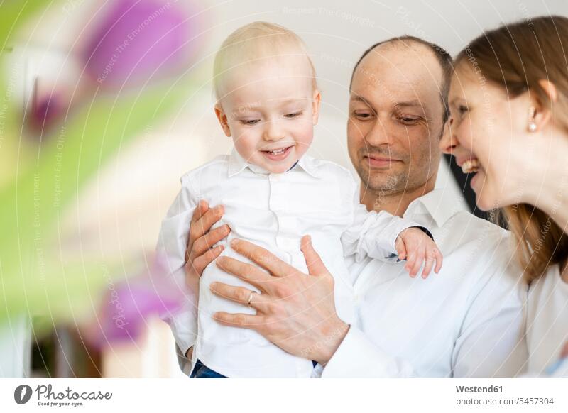 Smiling father holding baby boy while standing by cheerful mother at home color image colour image indoors indoor shot indoor shots interior interior view