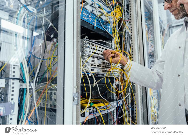 Mature man plugging in transceiver on fiber optic cable in data center color image colour image indoors indoor shot indoor shots interior interior view