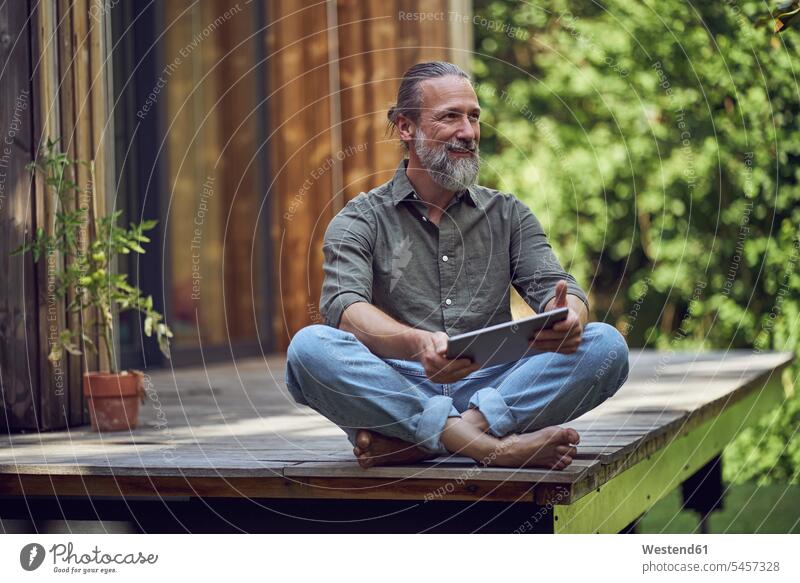 Bearded man with digital tablet contemplating while sitting outside tiny house color image colour image Germany leisure activity leisure activities free time