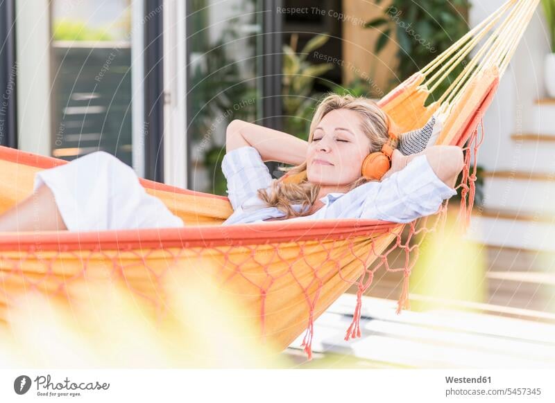 Portrait of mature woman with eyes closed lying in hammock on terrace listening music with headphones hammocks headset relax relaxing hear enjoy enjoyment