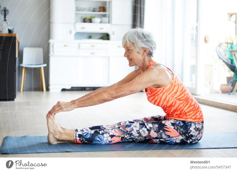 Fit senior woman stretching leg and back while exercising at home color image colour image indoors indoor shot indoor shots interior interior view Interiors day