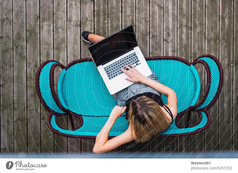 Young woman sitting on turquoise couch on terrace using laptop, top view Laptop Computers laptops notebook use Turquoise Color terraces females women settee