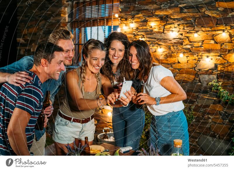 Happy friends meeting outdoors at a stone house taking a selfie mate Bottles Beer Bottles Tables telecommunication phones telephone telephones cell phone