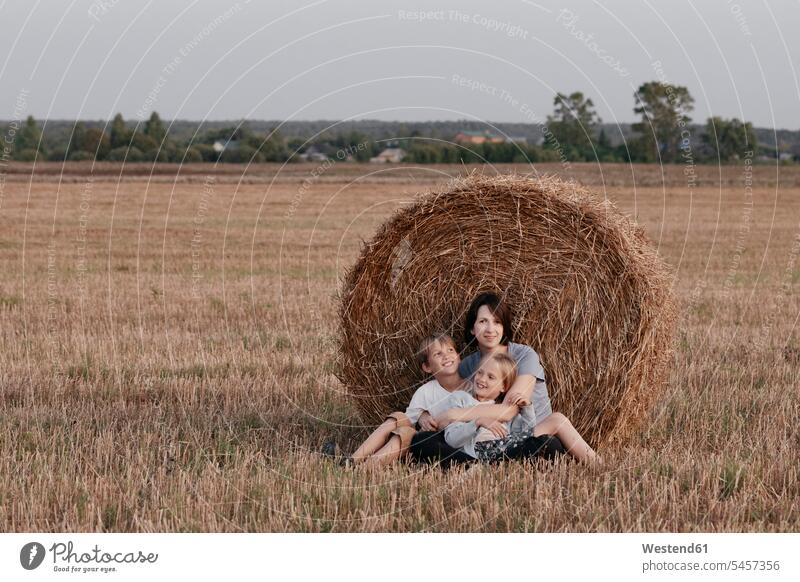 Woman with two kids sitting near a haystack on a stubble field day daylight rural scene series outdoor outdoors outside focus on foreground