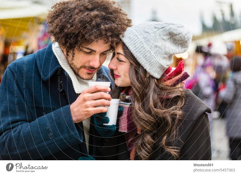Happy affectionate young couple with hot drinks at Christmas market Affection Affectionate twosomes partnership couples happiness happy hot beverage